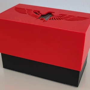 May include: A red box with a black base. The red lid features a carved eagle design. The box is rectangular and appears to be made of plastic or a similar material. The design is simple and modern.