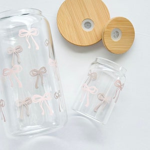 May include: Two glass jars with pink bow designs and bamboo lids. The larger jar has a wider mouth and the smaller jar has a narrower mouth.