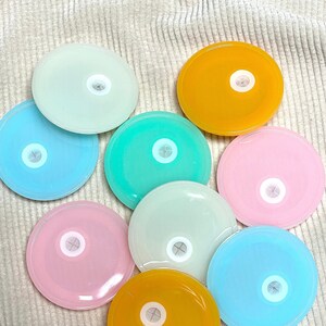 May include: Nine round, colourful lids with a small hole in the centre. The lids are in shades of blue, green, yellow, and pink.