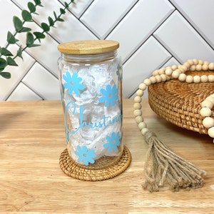 May include: A clear glass jar with a bamboo lid and a blue floral design. The jar is personalized with the name "Christina".