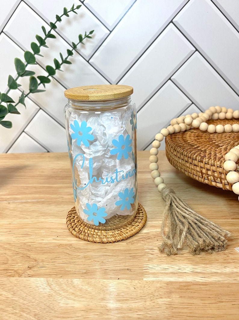May include: A clear glass jar with a bamboo lid and a blue floral design. The jar is personalized with the name "Christina".