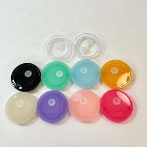 May include: Assortment of ten round, colourful lids with a small hole in the centre. The lids are in various colours, including black, green, blue, yellow, pink, and purple. Two clear plastic lids are also included.