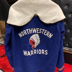 Puede incluir: Una chaqueta de béisbol azul con cuello blanco y un tocado de plumas de indio bordado en rojo y blanco con el texto "NORTHWESTERN WARRIORS" en la espalda.