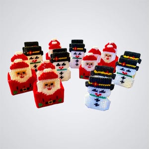 May include: A collection of handmade Christmas ornaments featuring Santa Claus and snowman designs. The Santa ornaments are red with white beards and hats, while the snowmen are white with black hats and coal eyes. The ornaments are made from a woven material.