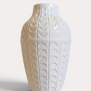 Puede incluir: Un jarrón de cerámica blanca con un patrón de hojas texturizadas y repetitivas. El jarrón tiene un cuerpo redondeado y un cuello estrecho. El diseño incluye una banda horizontal cerca de la parte superior. Este jarrón decorativo es adecuado para la decoración del hogar.