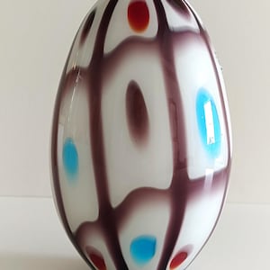 May include: White glass vase with a rounded shape and a geometric pattern of purple, red, and blue. The vase has a glossy finish.