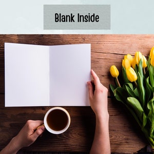 May include: A blank white card folded in half, with a cup of tea and a bouquet of yellow tulips on a wooden table. The card has the words "Blank Inside" printed on the front.
