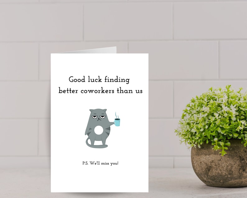 May include: A white card with a gray cat cartoon holding a blue cup of coffee. The text on the card reads "Good luck finding better coworkers than us." and "P.S. We'll miss you!"