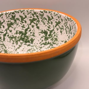 May include: A ceramic bowl with a dark green exterior and a white interior speckled with green. The rim is a bright orange colour. This bowl is suitable for serving food.
