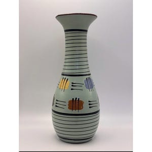 Peut inclure: Un grand vase en céramique vert clair avec un dessus évasé et une base arrondie. Le vase présente des rayures horizontales noires et des motifs abstraits colorés en jaune, marron et violet. Le bord est de couleur marron foncé.