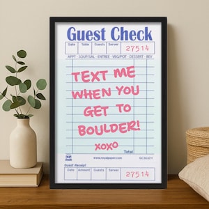 May include: A framed print resembling a guest check, featuring the text "TEXT ME WHEN YOU GET TO BOULDER!" in pink. The top section reads "Guest Check" with fields for date, table, guests, and server. A decorative piece for a home or office.