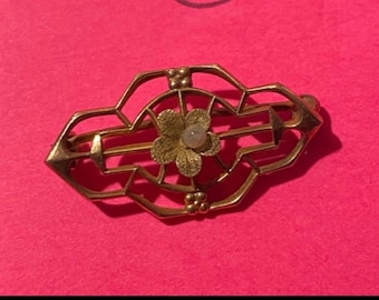 May include: A gold-toned brooch with a delicate floral design. The center of the flower features a small, white pearl.
