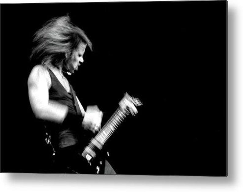 Puede incluir: Imagen en blanco y negro de una persona tocando una guitarra el&eacute;ctrica. La persona lleva una camiseta sin mangas negra y tiene el pelo largo. La guitarra est&aacute; enfocada, con la cara y el pelo borrosos por el movimiento.