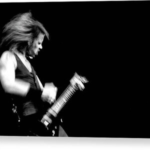 Puede incluir: Imagen en blanco y negro de una persona tocando una guitarra el&eacute;ctrica. La persona lleva una camiseta oscura sin mangas y tiene el pelo largo. La guitarra es negra con cuerdas plateadas, y el fondo es negro liso.