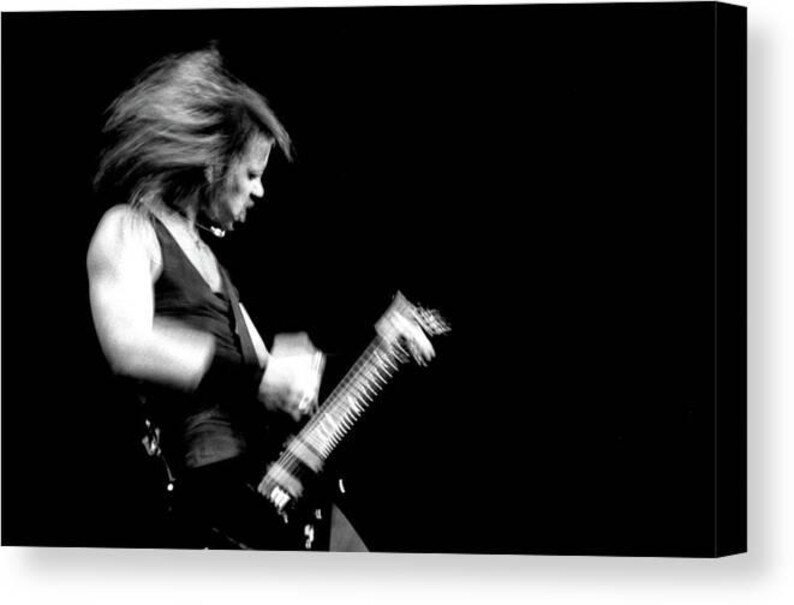 Puede incluir: Imagen en blanco y negro de una persona tocando una guitarra el&eacute;ctrica. La persona lleva una camiseta oscura sin mangas y tiene el pelo largo. La guitarra es negra con cuerdas plateadas, y el fondo es negro liso.