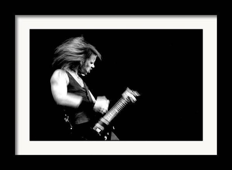 Puede incluir: Fotograf&iacute;a enmarcada en blanco y negro de una persona tocando una guitarra el&eacute;ctrica. La persona lleva una camiseta sin mangas y tiene el pelo largo. La imagen es un primer plano, con la persona y la guitarra enfocadas sobre un fondo oscuro.