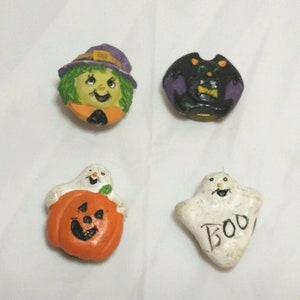 May include: Four Halloween themed ceramic buttons. A witch with a purple hat, a black bat, a ghost holding a pumpkin, and a ghost with the word "BOO" on it.