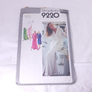 May include: A vintage Simplicity 9220 sewing pattern. The pattern features a woman in a white robe and illustrations of robes in pink, green, and blue. The pattern's cover is gray and white.