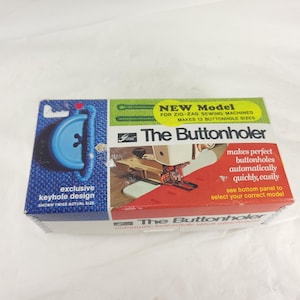 May include: A vintage box for "The Buttonholer" sewing machine attachment. The box features a blue button graphic and text that reads "exclusive keyhole design." The box also states it makes 13 buttonhole sizes.