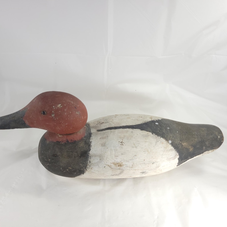 May include: A vintage wooden duck decoy, hand-painted with a red head, black beak, and a white and black body. The decoy is designed to float on water and attract other ducks. This decorative item is a classic piece of Americana.