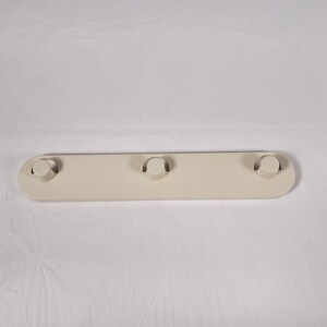 May include: A white plastic shelf bracket with three round holes. The bracket is designed to be mounted to a wall or other surface.