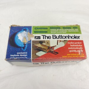 May include: A vintage box for "The Buttonholer" sewing machine attachment. The box features a blue keyhole design graphic and text that reads "exclusive keyhole design." The box also shows a sewing machine in action and states that it makes perfect buttonholes automatically.
