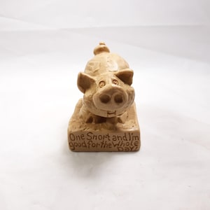 May include: A beige ceramic figurine of a pig with a toothy grin. The pig is standing on a rectangular base with the text "One Smart and I'm good for the whole day!"