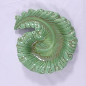 May include: A green ceramic dish shaped like a leaf with a swirl design. The dish has a glossy finish and is perfect for serving snacks or holding jewelry.