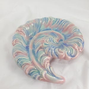 May include: A ceramic, nautilus-shaped decorative piece. The sculpture features a swirling design with pastel colors, including pink, blue, and green. The glossy finish enhances the intricate details of the spiral form, creating a unique home decor item.