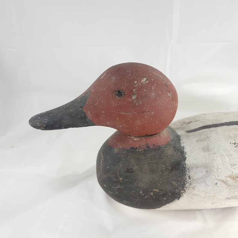May include: A vintage wooden duck decoy with a red head, black beak, and black neck. The body is painted white with black accents. The decoy is likely used for hunting or decorative purposes.