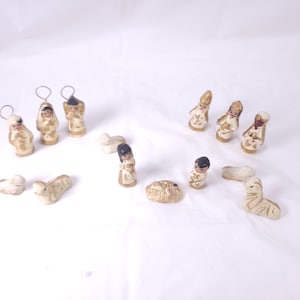 May include: A collection of small, hand-painted nativity scene figurines. The set includes figures of angels, the three wise men, Mary, Joseph, baby Jesus in a manger, and several sheep. The figurines are primarily beige with gold and brown accents.
