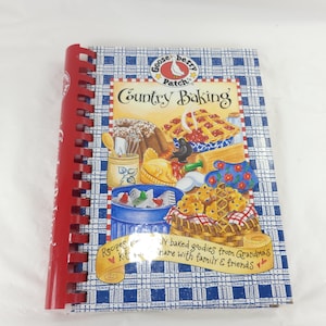 May include: A spiral-bound cookbook titled Country Baking by Gooseberry Patch. The cover features a blue and white checkered pattern with illustrations of baked goods, a basket, and kitchen tools. Text reads: Recipes and freshly-baked goodies from Grandma's kitchen to share with family & friends.