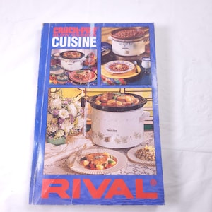 May include: A blue cookbook with the title "Crock-Pot Slow Cooker Cuisine" and the word "RIVAL" in red letters on the front cover. The cover features photos of three different slow cookers with various dishes inside.