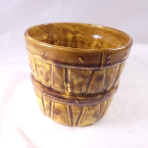May include: A brown ceramic planter with a barrel design. The planter has a wide opening and a textured surface that mimics wooden planks. The rim and bands are a darker shade of brown, and the planter is approximately 4 inches tall.