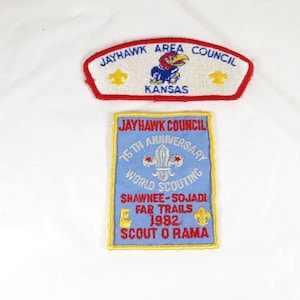 May include: Two blue and red embroidered patches with the text "Jayhawk Area Council Kansas" and "Jayhawk Council 75th Anniversary World Scouting Shawnee-Sojadi Far Trails 1982 Scout O Rama".