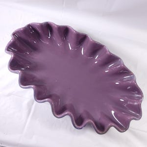 May include: A large, oval-shaped serving dish with a ruffled edge. The dish is made of ceramic and is a deep purple color.