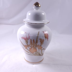 May include: White porcelain jar with a gold lid and a floral design featuring orange and pink irises and a butterfly.