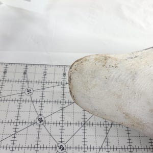 May include: A white, rounded object with a textured surface and brown spots, possibly a shoe last, is positioned near a ruler with black markings. The ruler has degree angles marked at 15, 30, and 45 degrees.