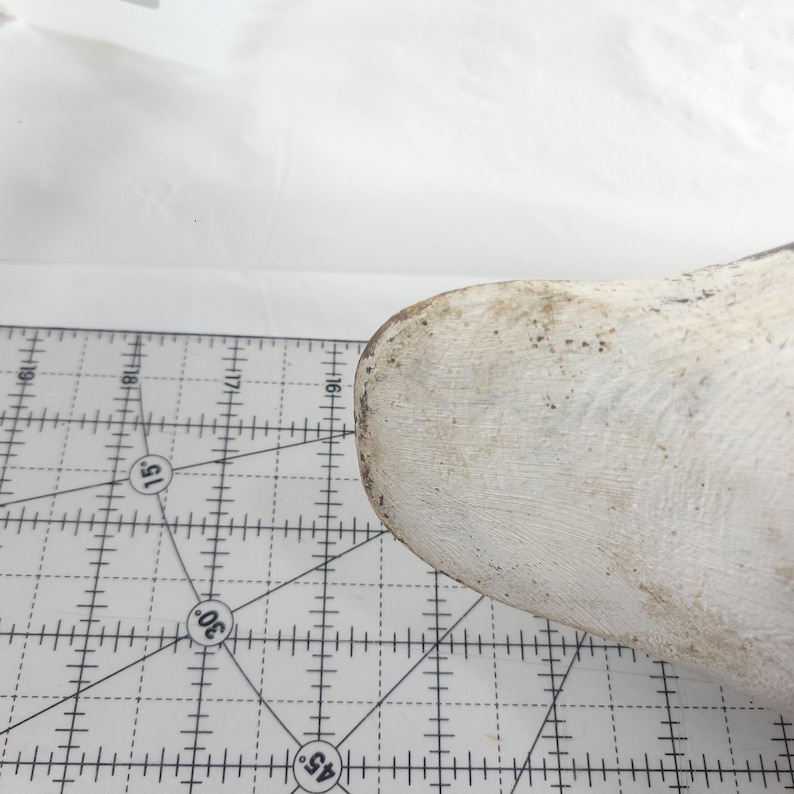 May include: A white, rounded object with a textured surface and brown spots, possibly a shoe last, is positioned near a ruler with black markings. The ruler has degree angles marked at 15, 30, and 45 degrees.