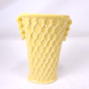May include: A yellow ceramic vase with a basket weave design. The vase has two decorative handles and a slightly flared rim. The vase is approximately 8 inches tall.