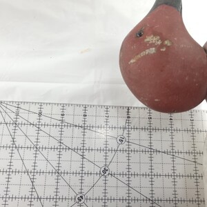 May include: A vintage wooden bird figurine with a red body and black head. The bird's body shows signs of wear, with visible paint chipping. A ruler is in the foreground, with measurements in inches.