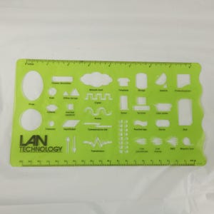 May include: A green plastic stencil with various network and technology symbols, including a cloud, telephone, and server. It has a ruler along the bottom edge, marked in inches. The text "LAN TECHNOLOGY" is printed on the stencil.