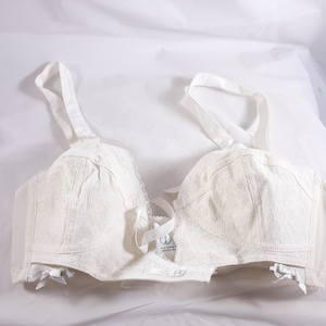 May include: White lace bra with adjustable straps and a bow detail in the center. The bra has a hook and eye closure in the back.