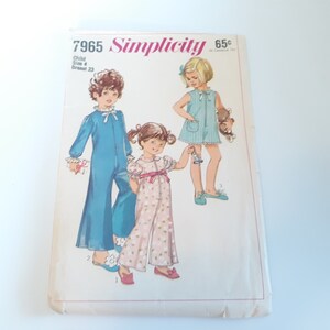 May include: Vintage Simplicity sewing pattern number 7965 for children's pajamas. The pattern includes three different styles: a blue jumpsuit, a pink floral jumpsuit, and a blue and white striped dress. The pattern is for a child size 4 with a 23 inch bust.