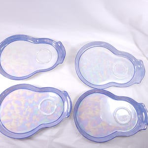 May include: Four iridescent, oval-shaped serving dishes with a light blue rim and a small, circular indentation in the center. The dishes have a pearlescent sheen, reflecting various colors. The overall design is simple and elegant.