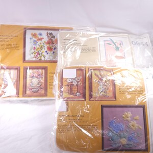 May include: Several cross-stitch kits are visible, featuring floral designs in wooden frames. The kits include images of flowers, butterflies, and vases. The text on the packaging includes the names "Sunshine Garden", "Collection", and "Enchanted Garden".