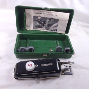 May include: Vintage Singer buttonholer attachment in a green plastic case. The black buttonholer has a white dial with a red "S" logo and the Singer brand name. The case contains instructions and accessories.
