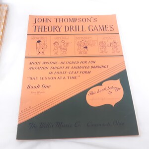 May include: A vintage orange and green book titled "John Thompson's Theory Drill Games". The book cover features cartoon illustrations and the text "Music Writing - Designed for Fun Notation Taught by Animated Drawings in Loose-Leaf Form "One Lesson at a Time" Book One".