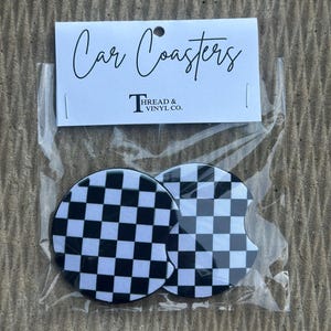 May include: Two car coasters with a black and white checkered pattern are displayed in a clear plastic package. The packaging includes a white label with the words "Car Coasters" and the "Thread & Vinyl Co." logo.