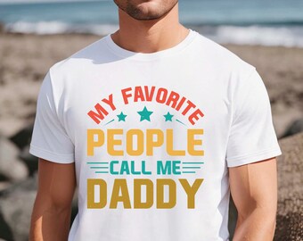 May include: White t-shirt with the text "MY FAVORITE PEOPLE CALL ME DADDY" in orange, yellow, teal, and gold. The design includes stars and is centered on the chest. The shirt is short-sleeved.